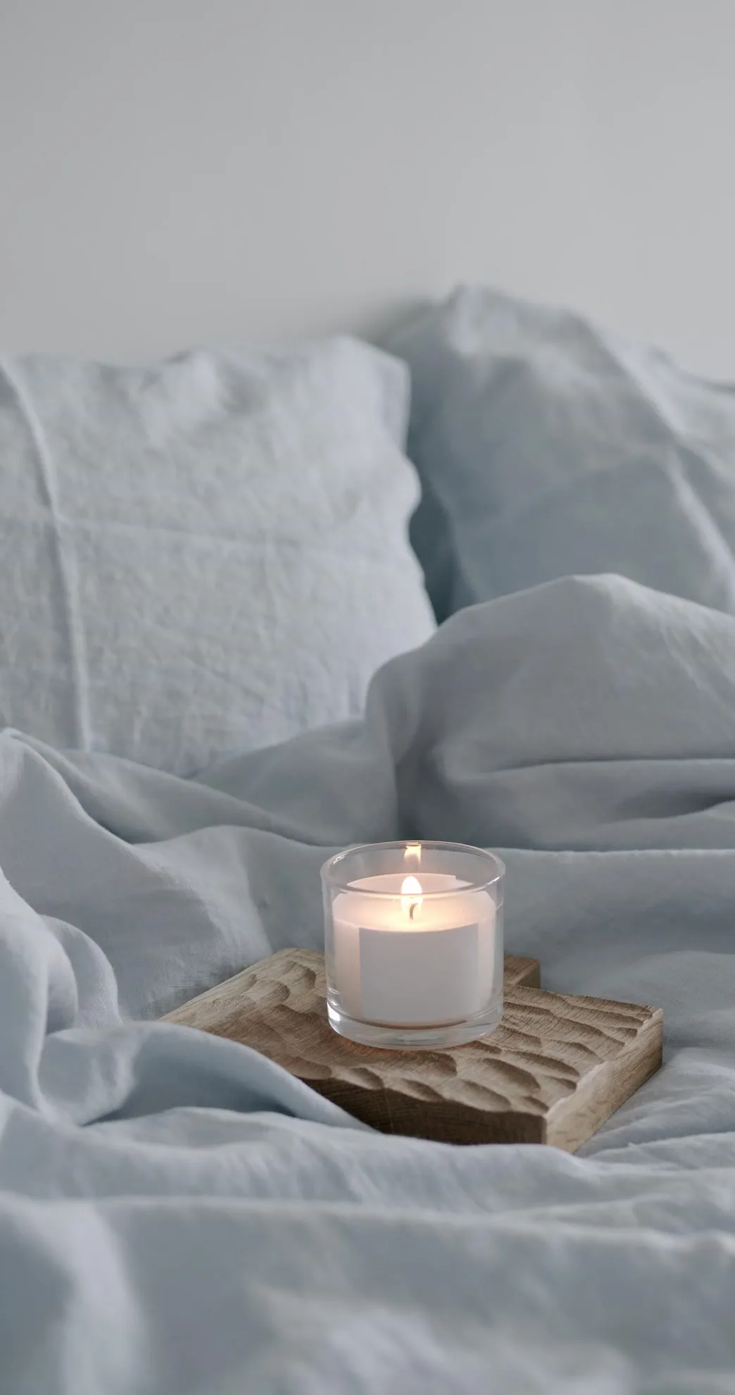 Lit candle on a carved wooden block against soft linen